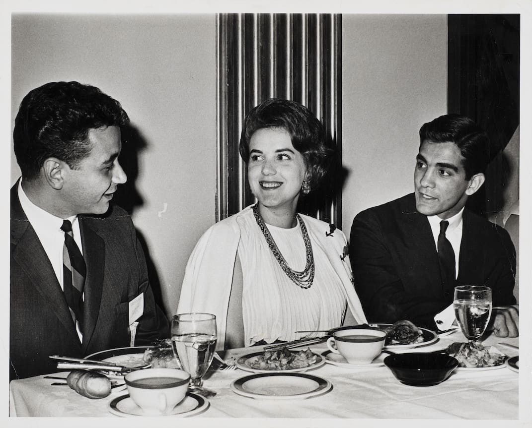 Two men and a woman talking at a dining table.