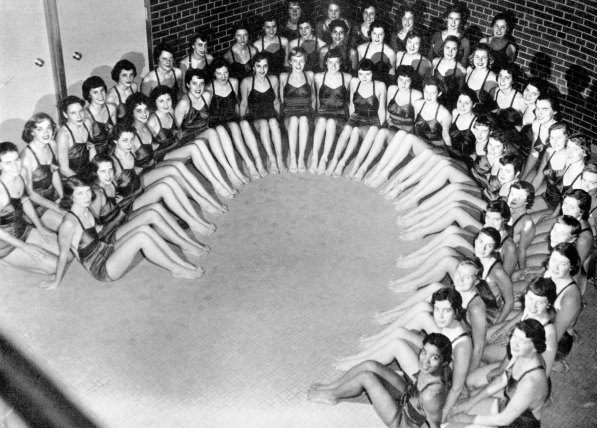 Group picture of the Women's Synchronized Swimming team sitting together in a U formation.