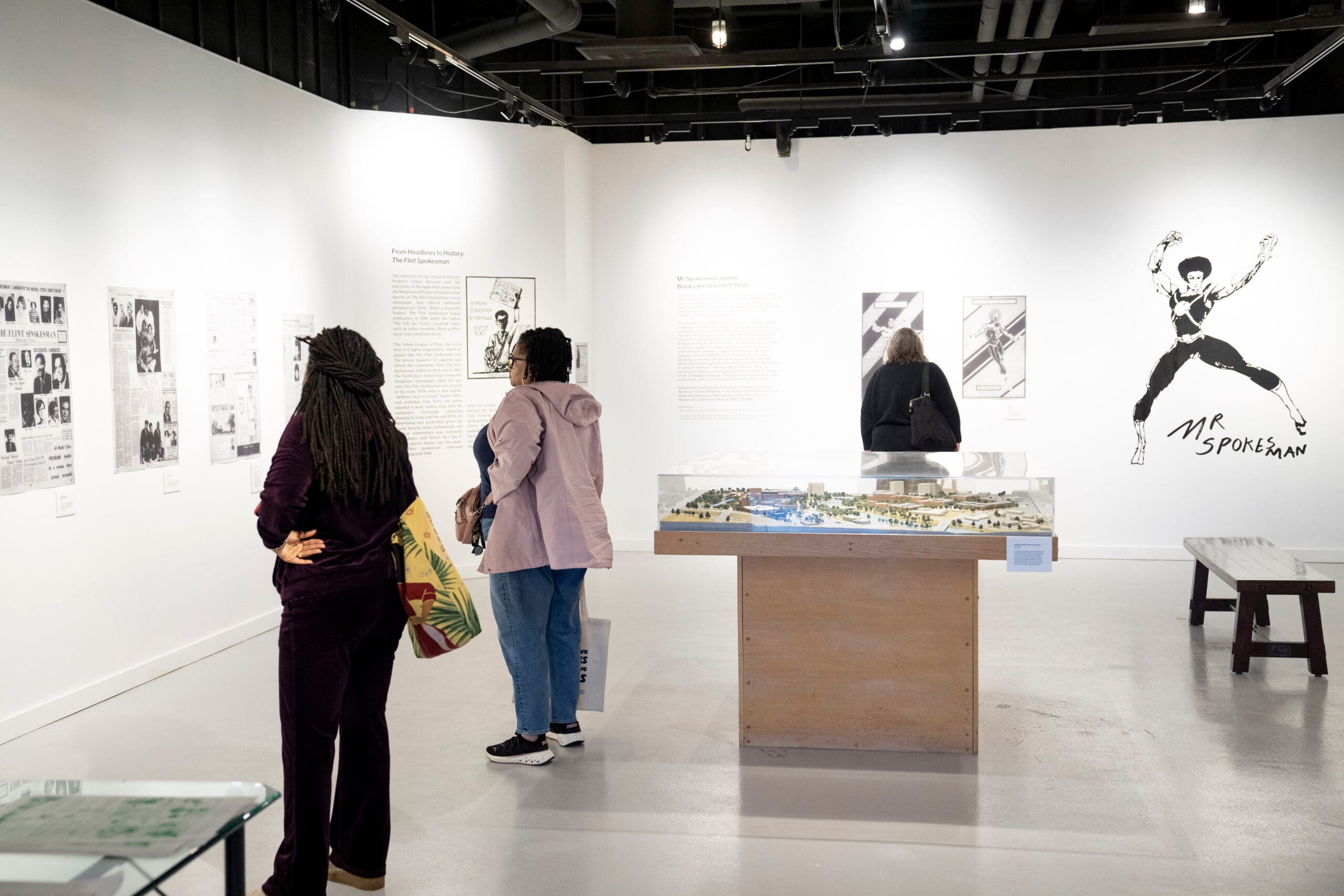 People standing in an exhibit space looking at prints of newspapers on the walls.