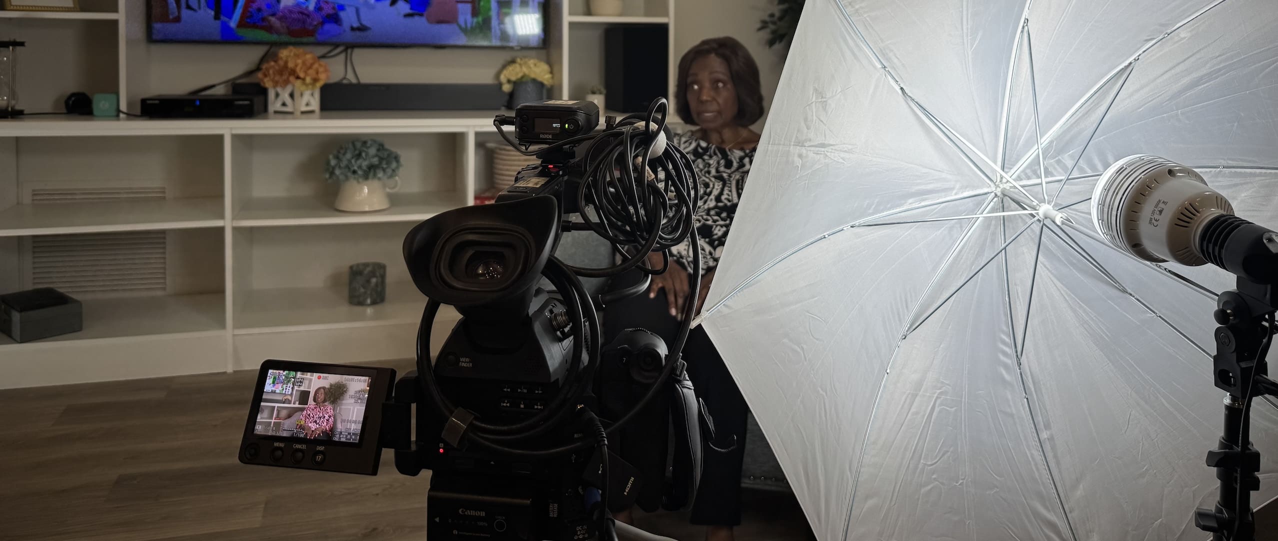 A camera and umbrella light turned taping the interivew Blenda Wilson, who sits in front of a bookshelf.