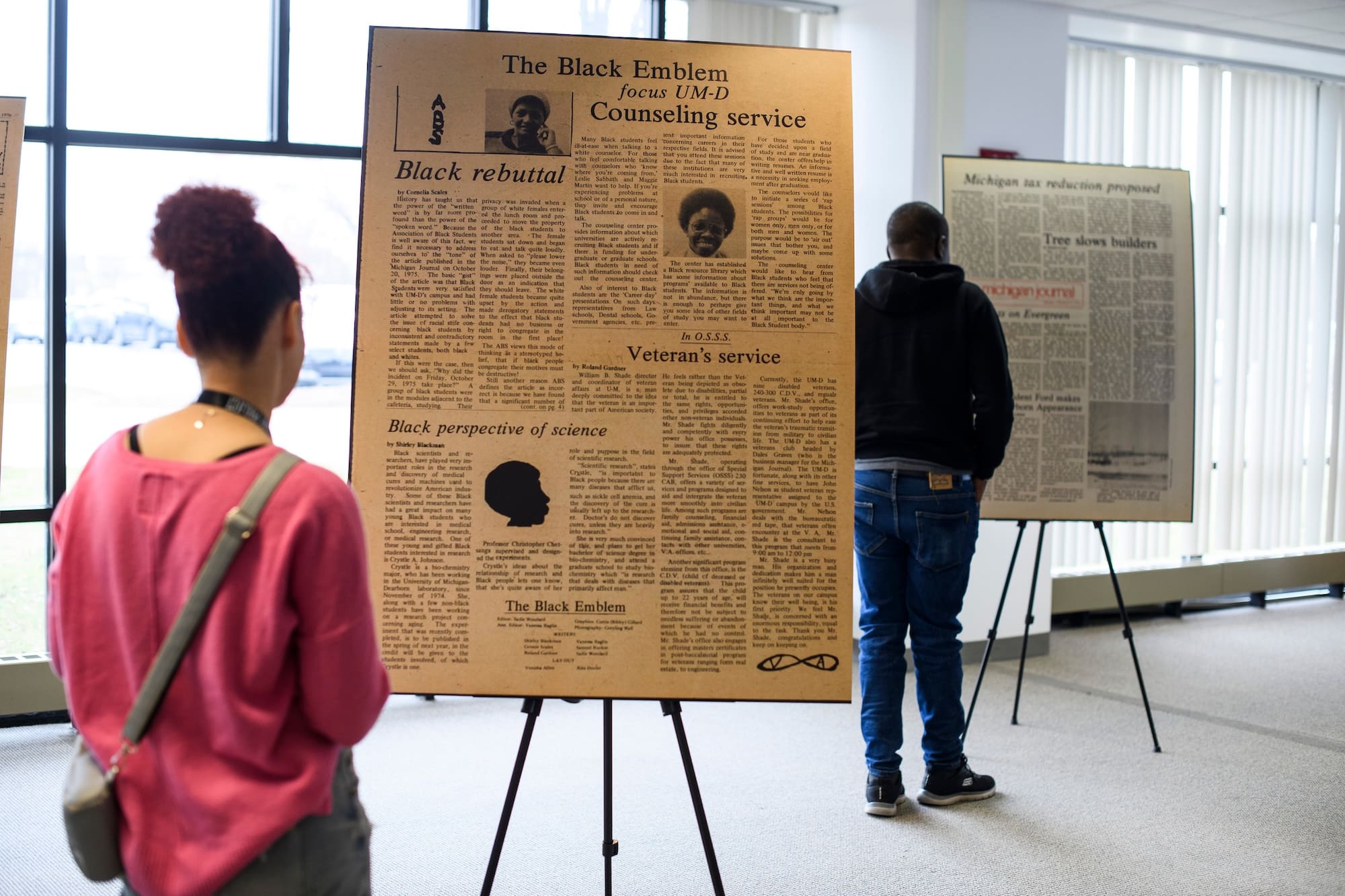 Woman looks at a poster on an easel and man looks at other poster in the background.