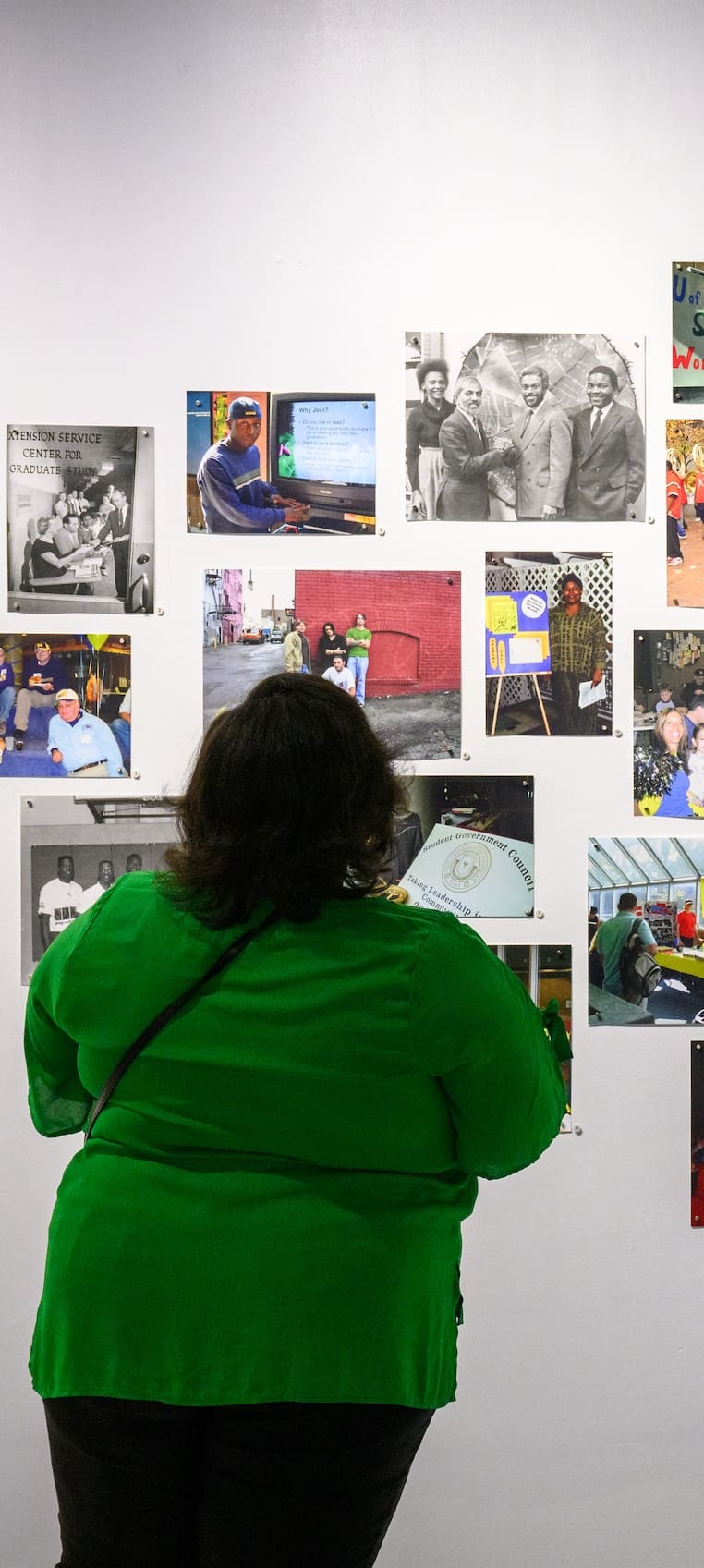 Woman in green examines photographs on wall at exhibit.