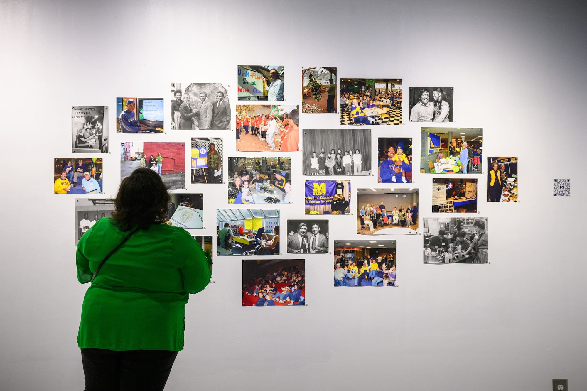 Woman in green examines photographs on wall at exhibit.