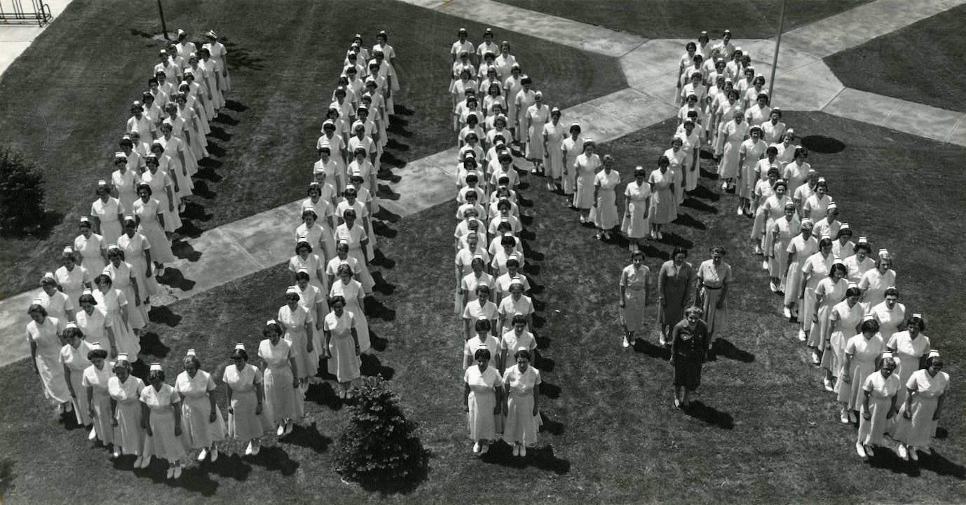 Group photo of the University of Michigan School of Nurses Class of 1960 wearing their nurse's uniforms and standing in a "UM" formation on the campus diag.