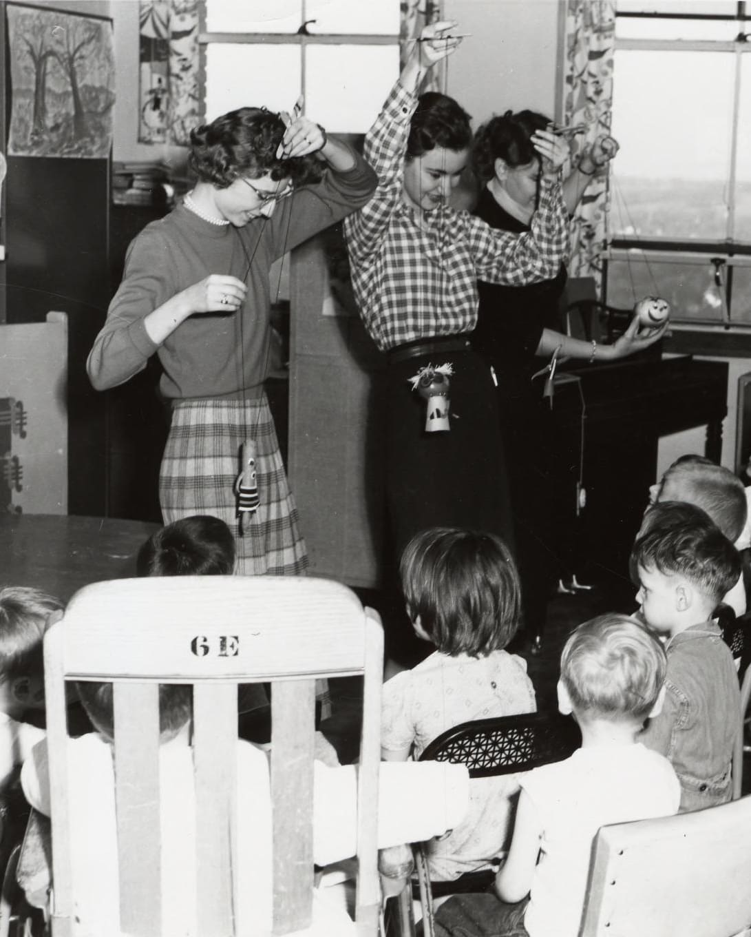 Three women teachers at the University of Michigan Hospital School playing with marionettes in front of a group of young children.