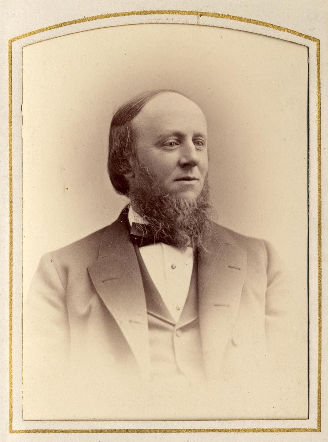 Man with a beard wearing a suit coat, best and bow tie.