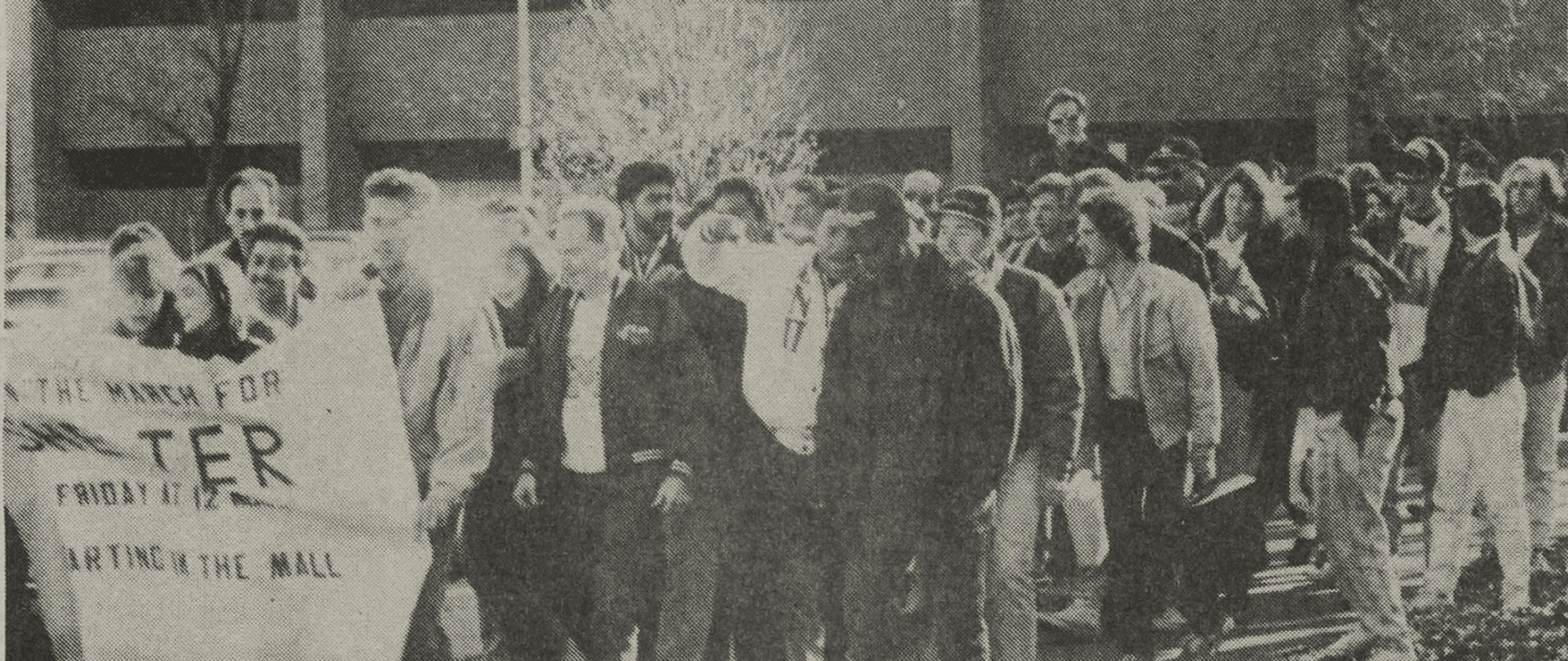 A group of UM-Dearborn students march behind a protest banner outside the UM-Dearborn Mardigian Library.