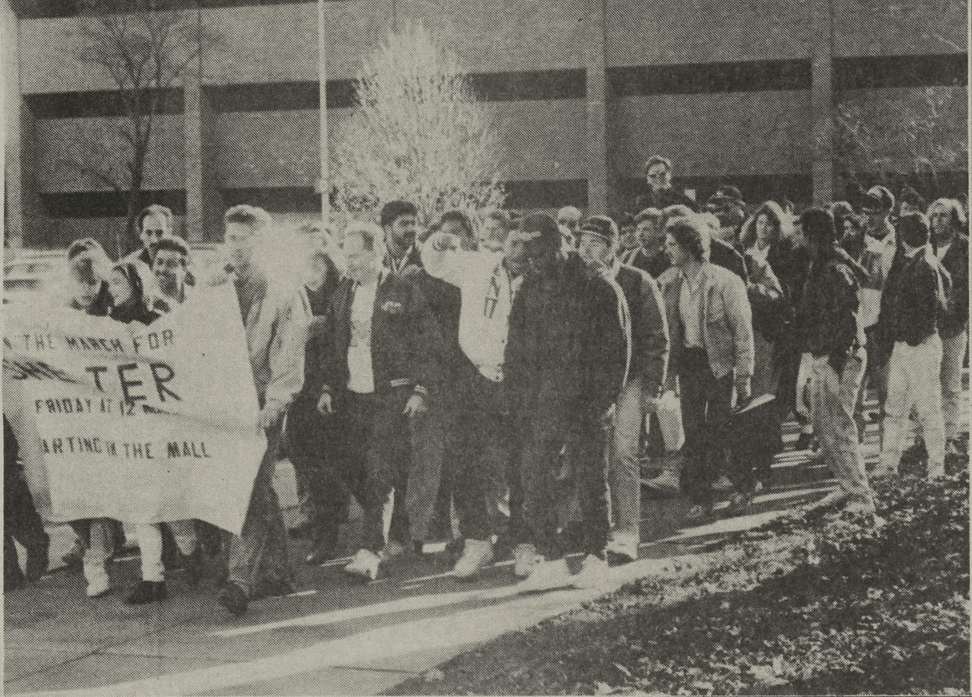 A group of UM-Dearborn students march behind a protest banner outside the UM-Dearborn Mardigian Library.
