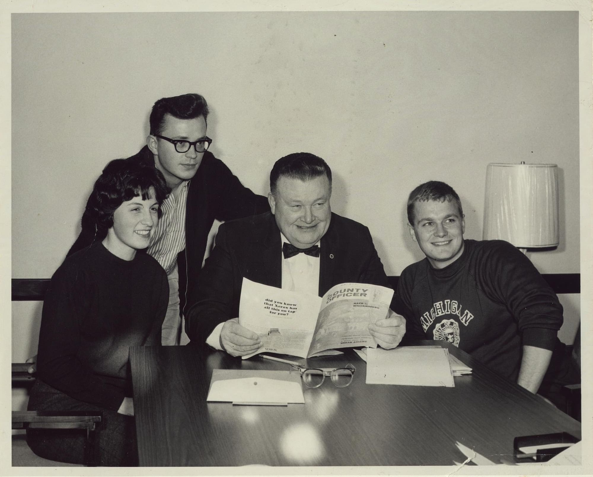 Mayor Orville Hubbard at a table with three college students, holding a paper.