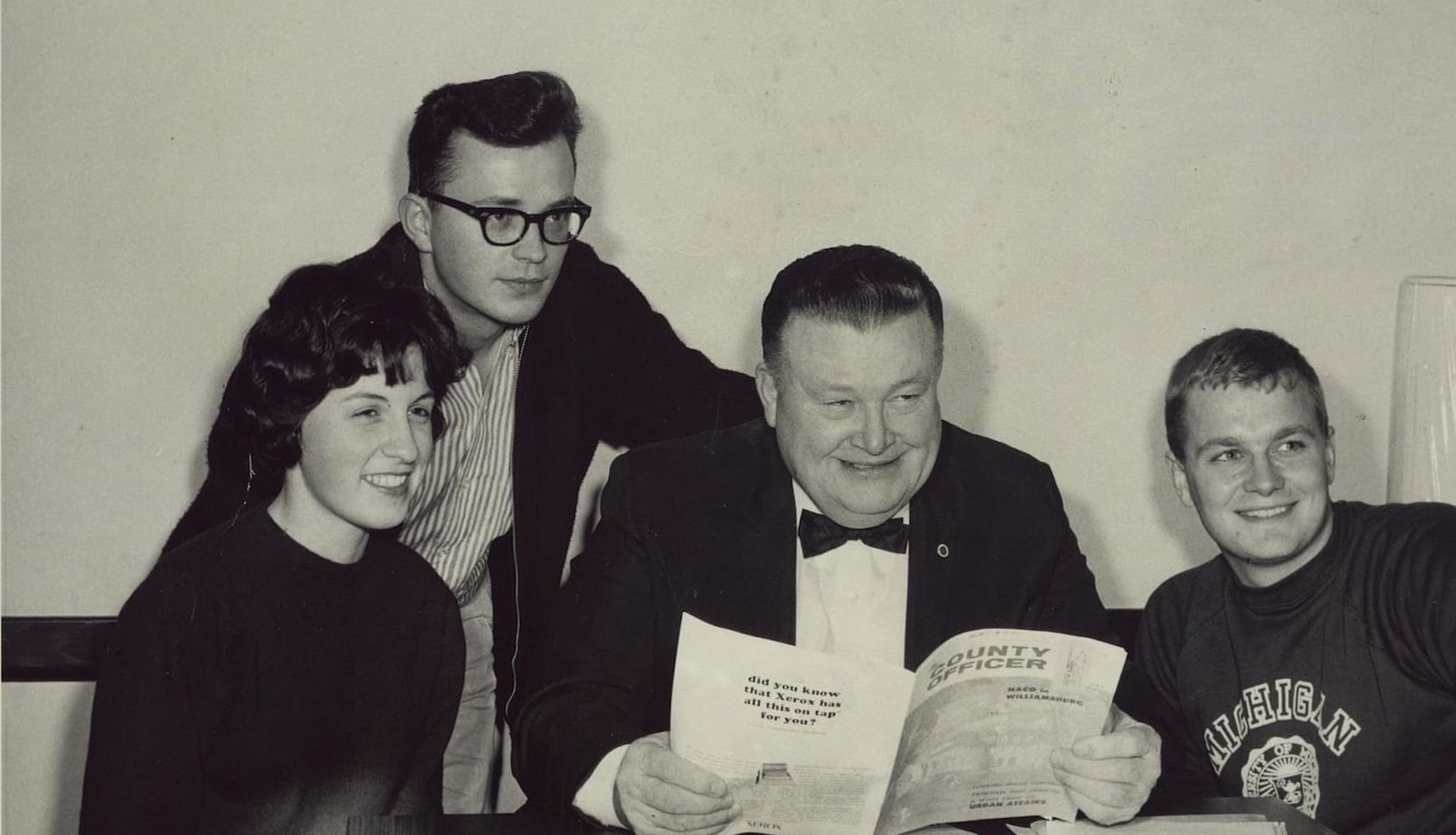 Mayor Orville Hubbard at a table with three college students, holding a paper.